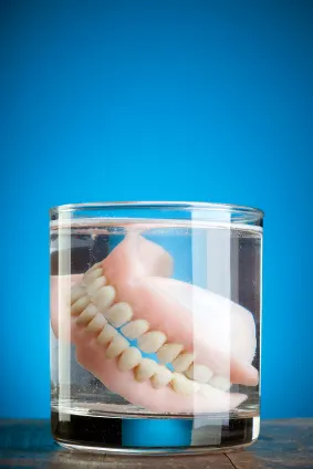 Dentures soaking in a glass full of water blue background